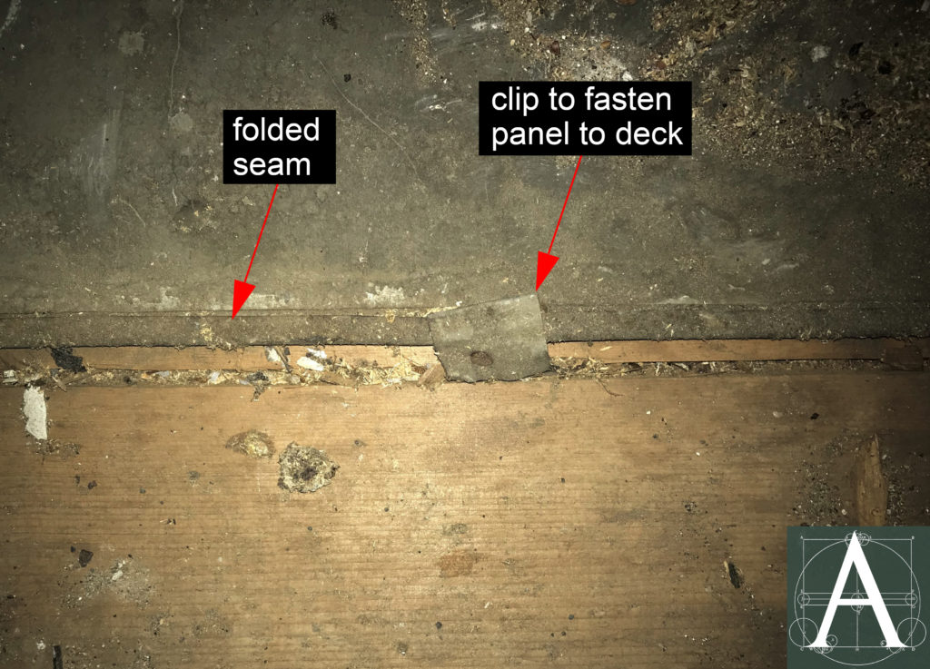 Tin-plated roof panel showing a clip to fasten it to the roof deck and the open half of an interlocking seam between panels